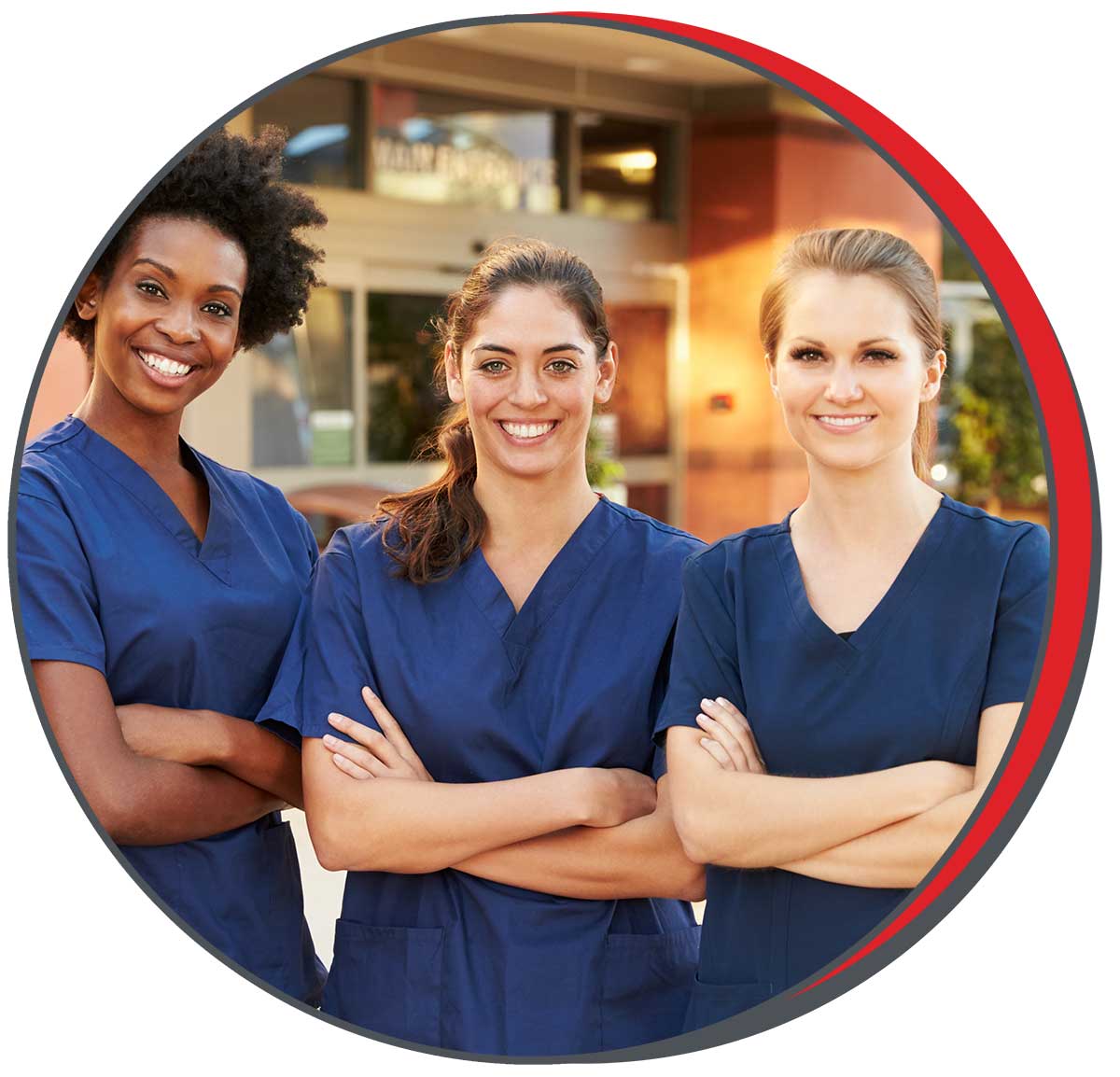 Three smiling female nurses in navy scrubs standing confidently outside a healthcare facility