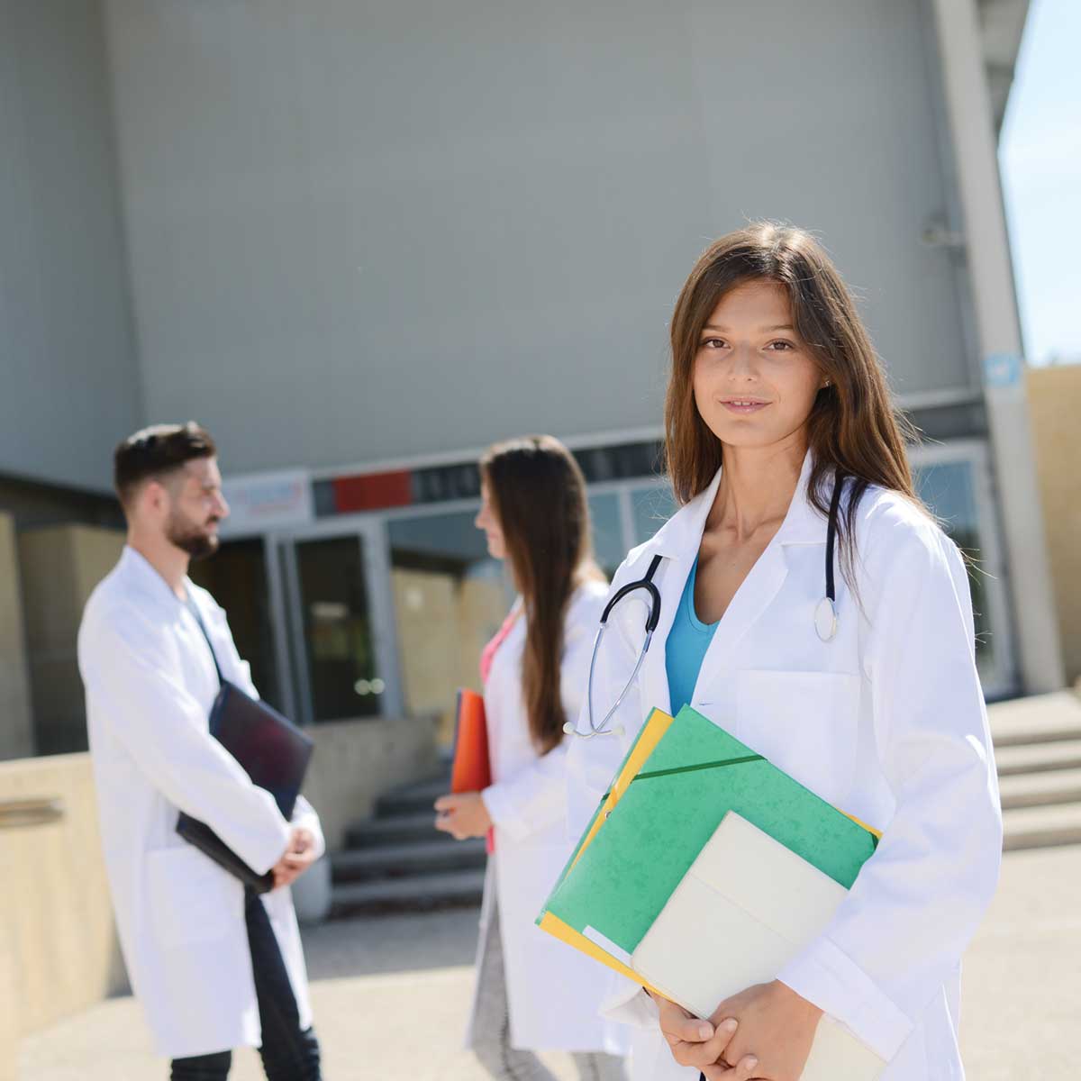 Female doctor in Clay County holding folders in front of a hospital building with other staff in the background